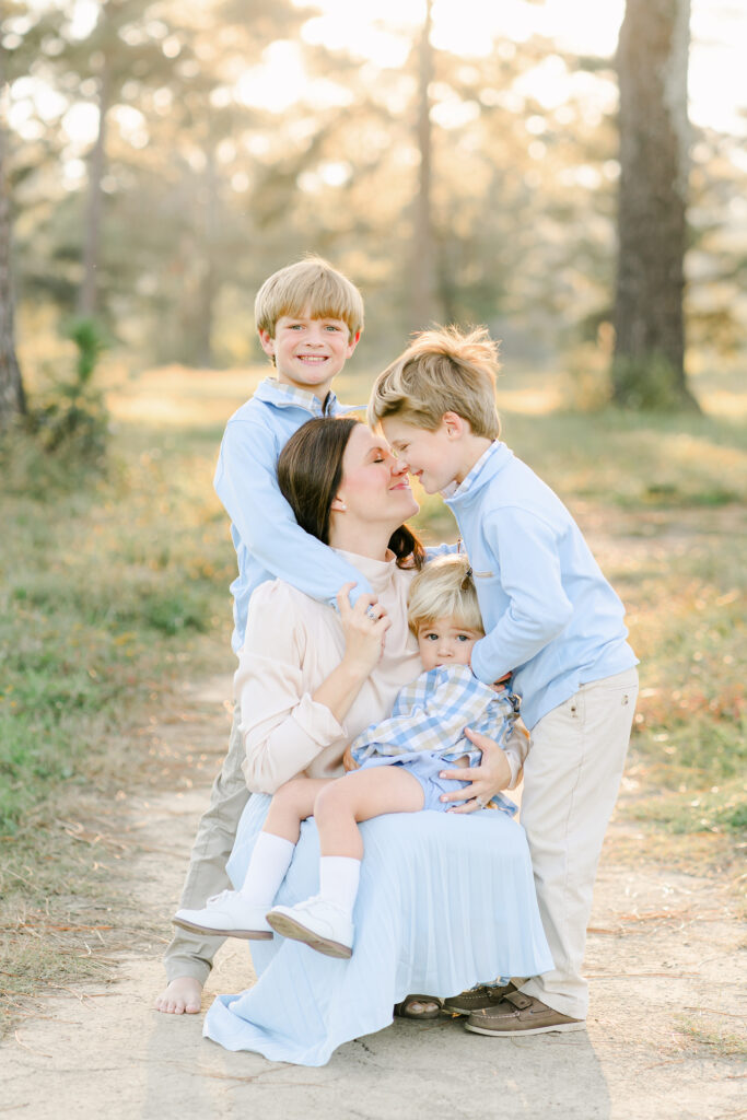 3 children hugging on their mom for a picture in a backlit field.