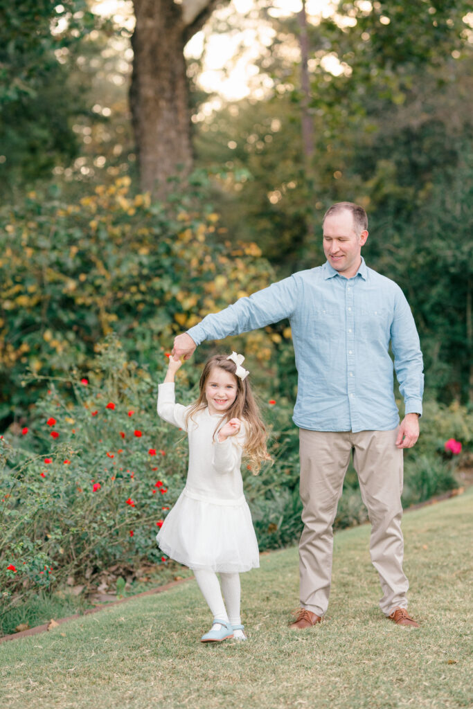 A dad  twirling his smiling daughter in a green garden.