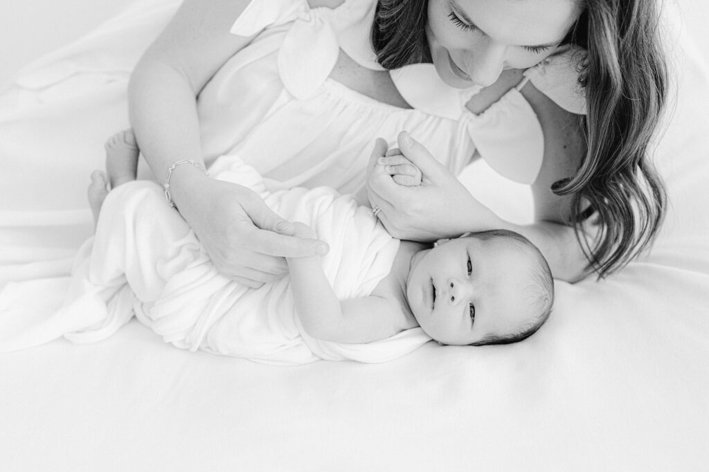 A new mom snuggles her newborn on a bed during a photo session in a white room.