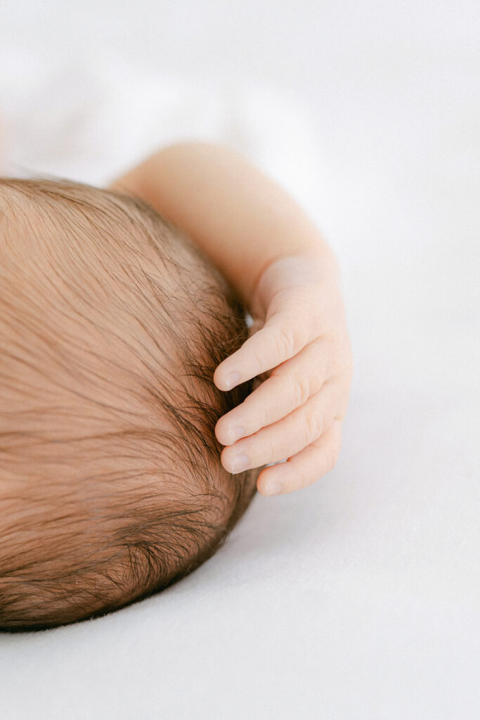 photo of a newborns head and hand while laying on a white blanket.