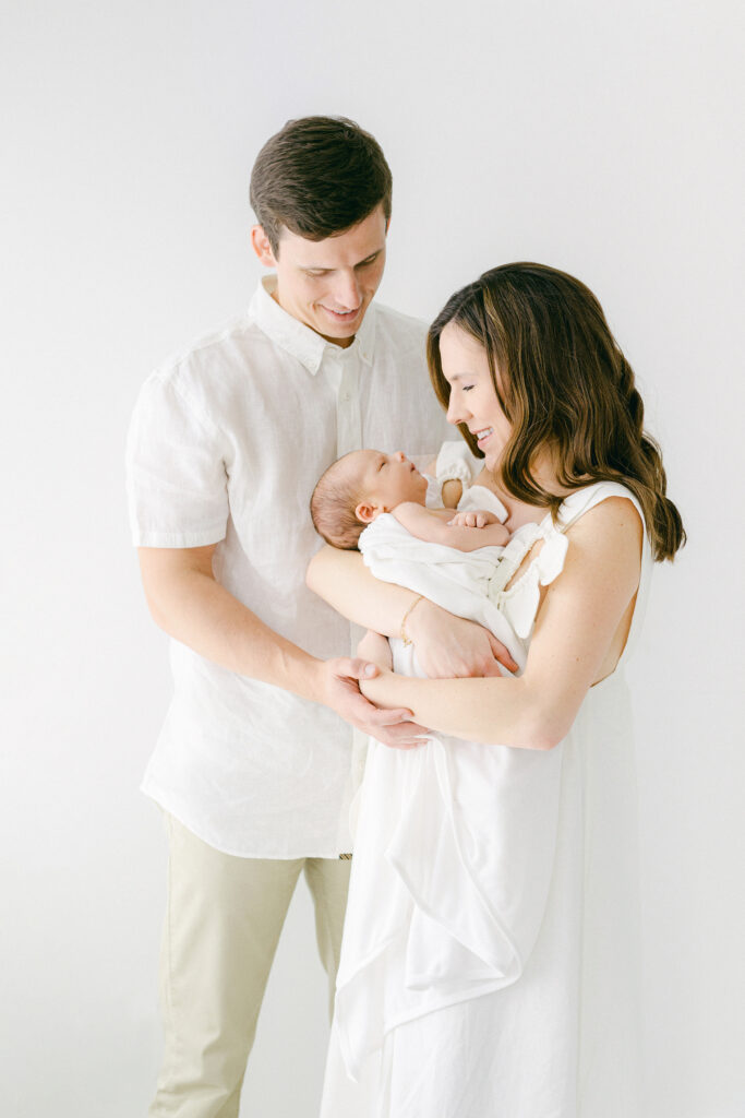 A new mom and dad snuggle their newborn during a photo session in a white room.