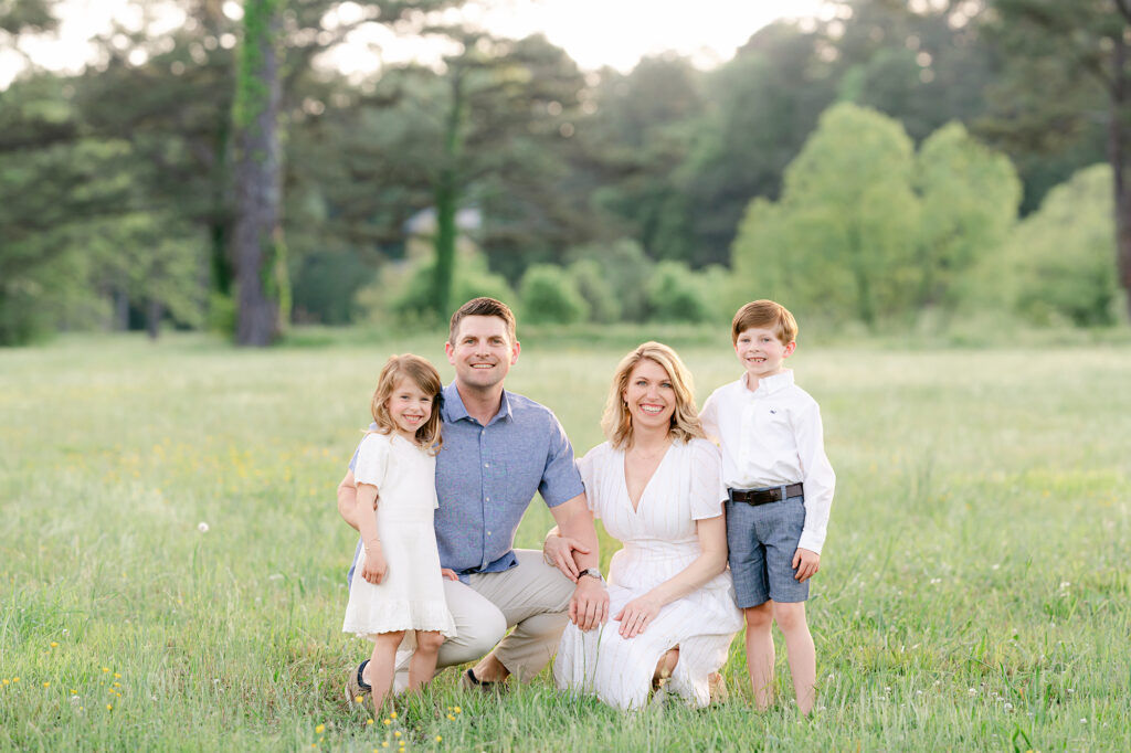 a family of 4 pose, while kneeling in a green field