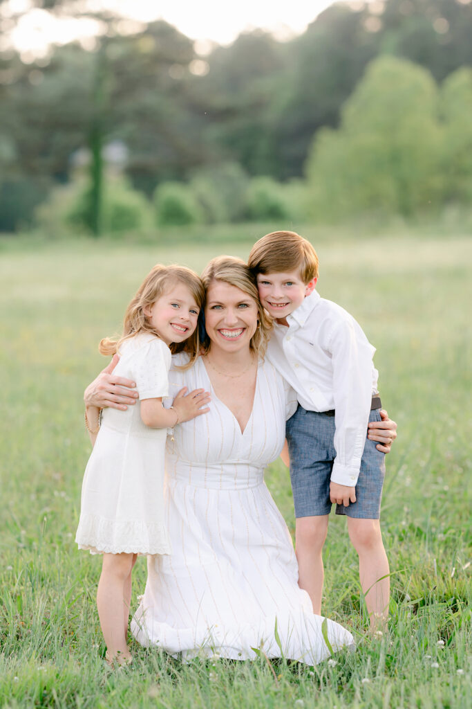 a mother hugs her young daughter and son during a photo session in a sunlit field