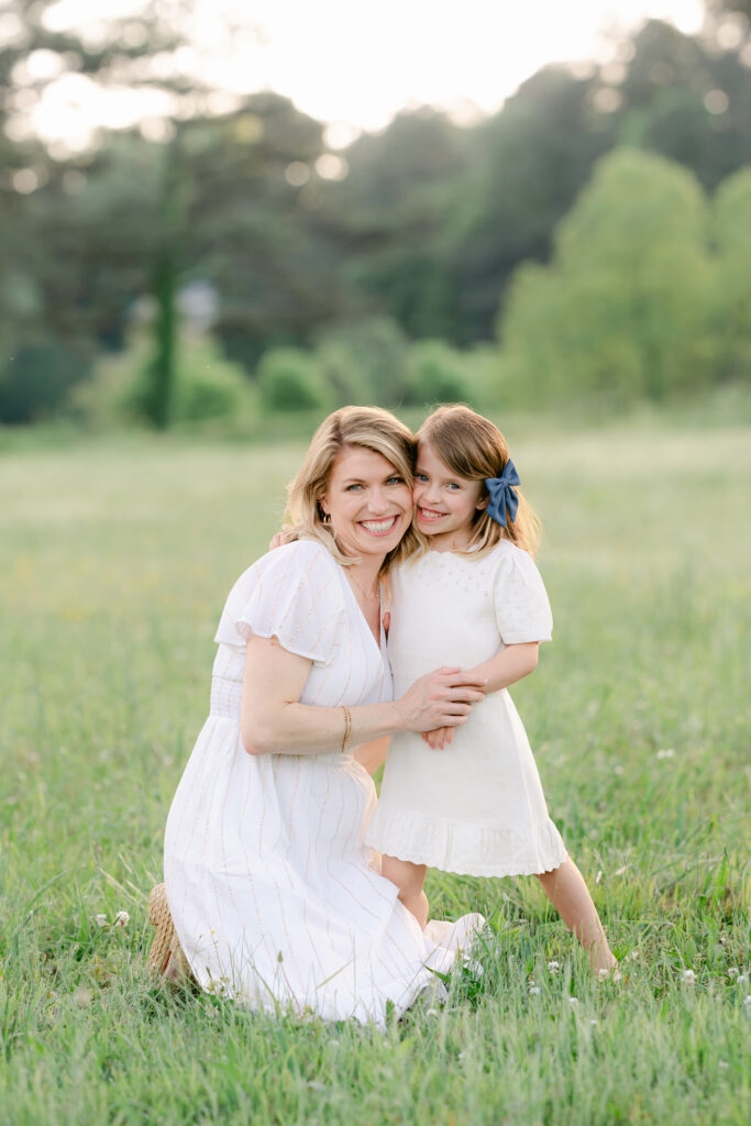 a mother hugs her young daughter during a photo session in a sunlit field