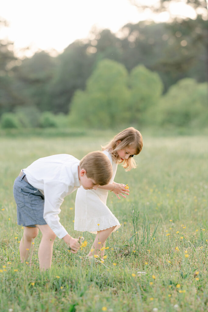 a young boy and girl pick yellow flowers in a green field