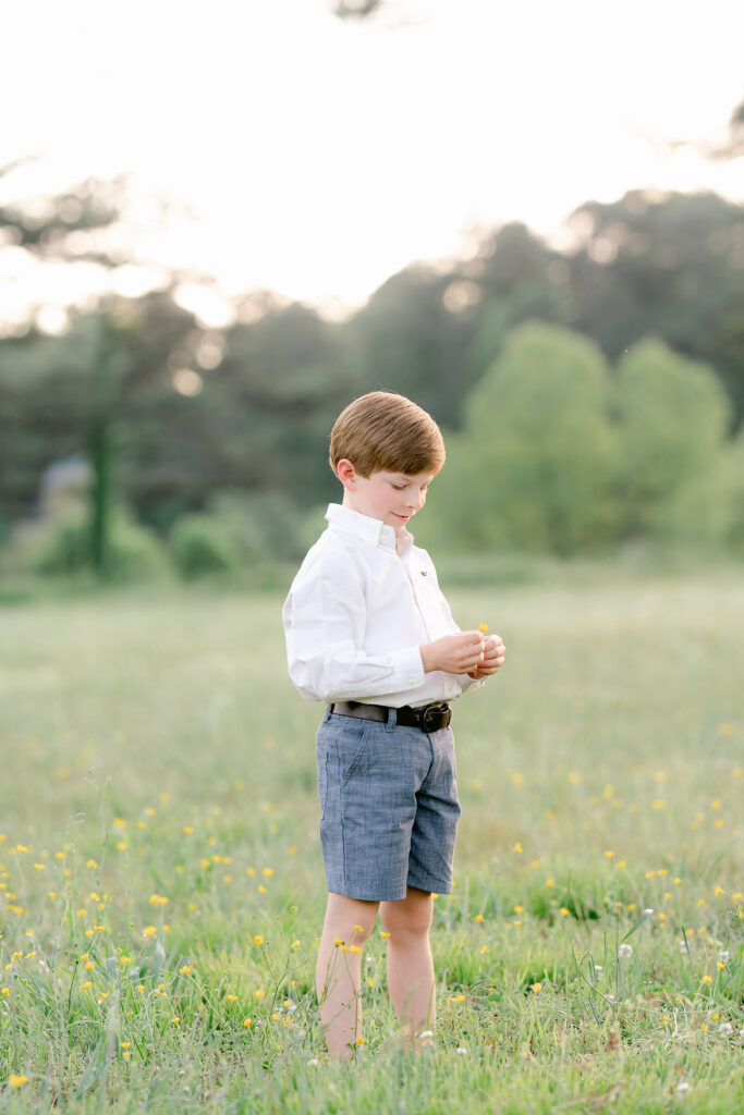 a young boy admires a yellow flower in a  greenfield