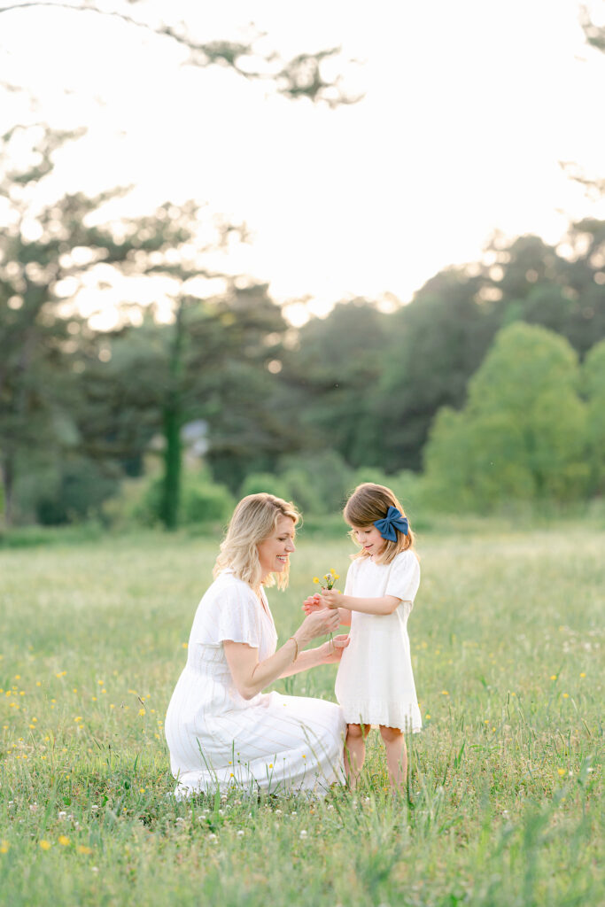 a mom and young daughter admire the girls yellow flower bouquet  in a  green field