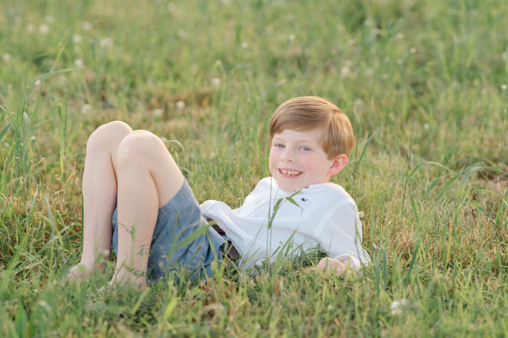 a young boy lays on the grass while smiling for the camera