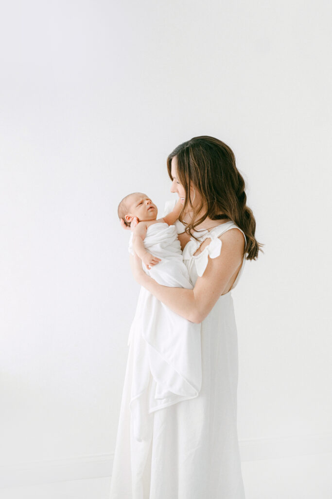 A new mom snuggles her newborn during a photo session in a white room.