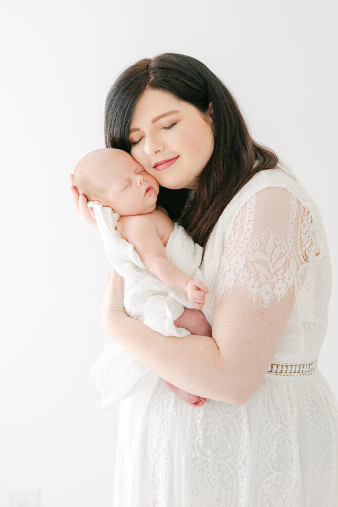 Photo of a mom holding her newborn baby, girl cheek to cheek.