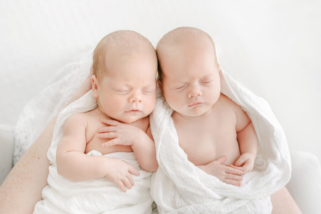 Photo of newborn twin girls from above in their mother's hands.  The babies are asleep.