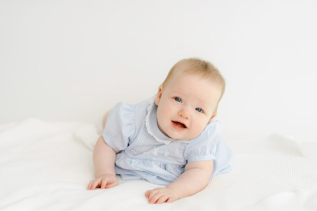 A 7 month old baby girl has her photo taken on a white bed.    