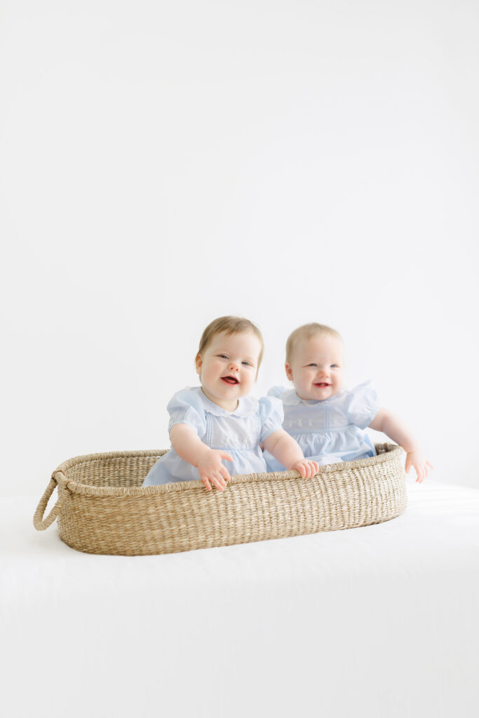 A photo of twin girls sitting in a basket happily smiling for the camera.