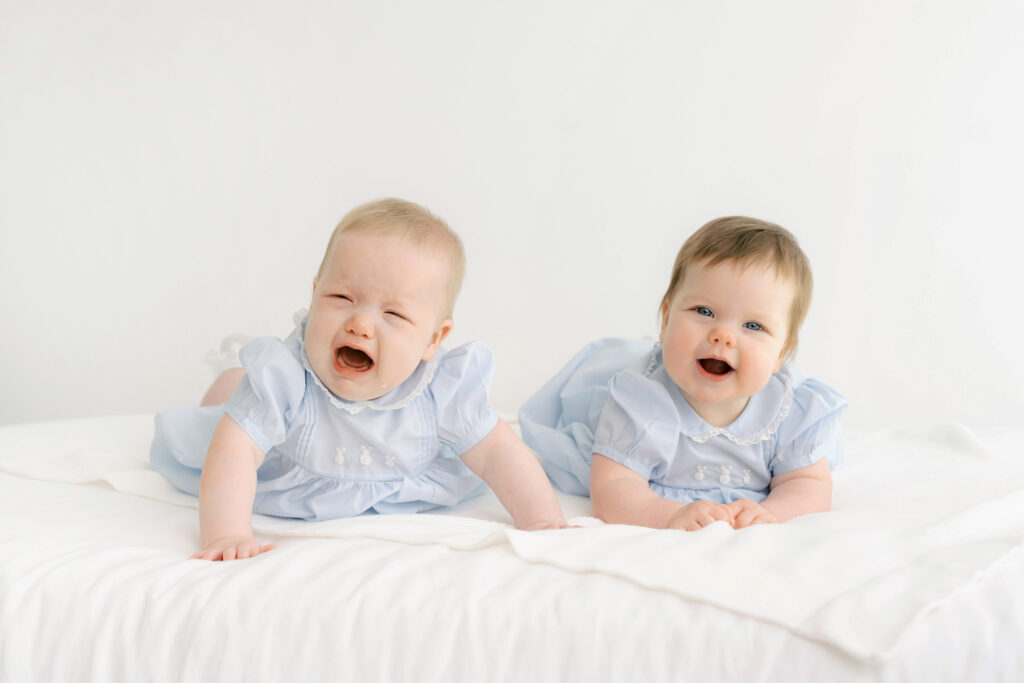 Twin girls have their photo taken on a white bed.  