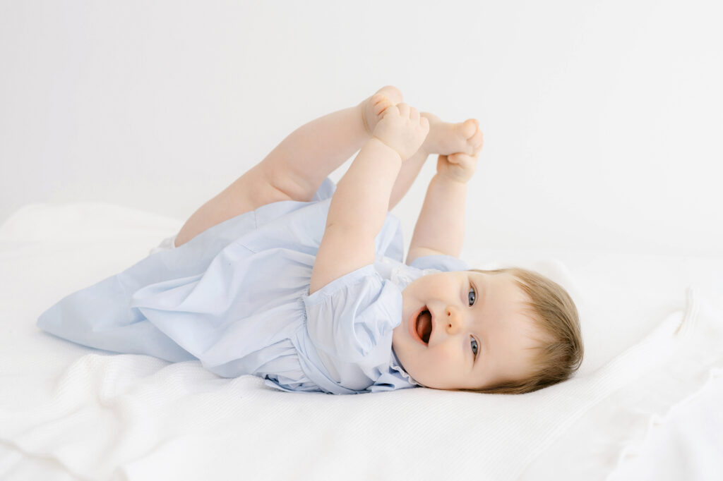 A 7 month old baby girl has her photo taken on a white bed.    