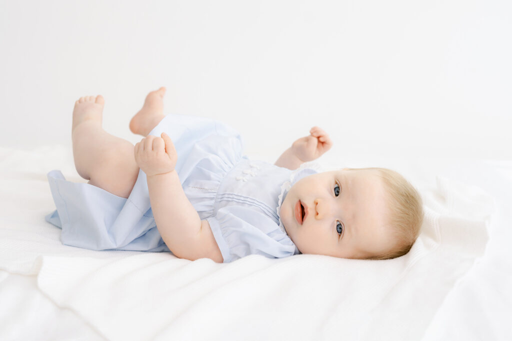 A 7 month old baby girl has her photo taken on a white bed.    