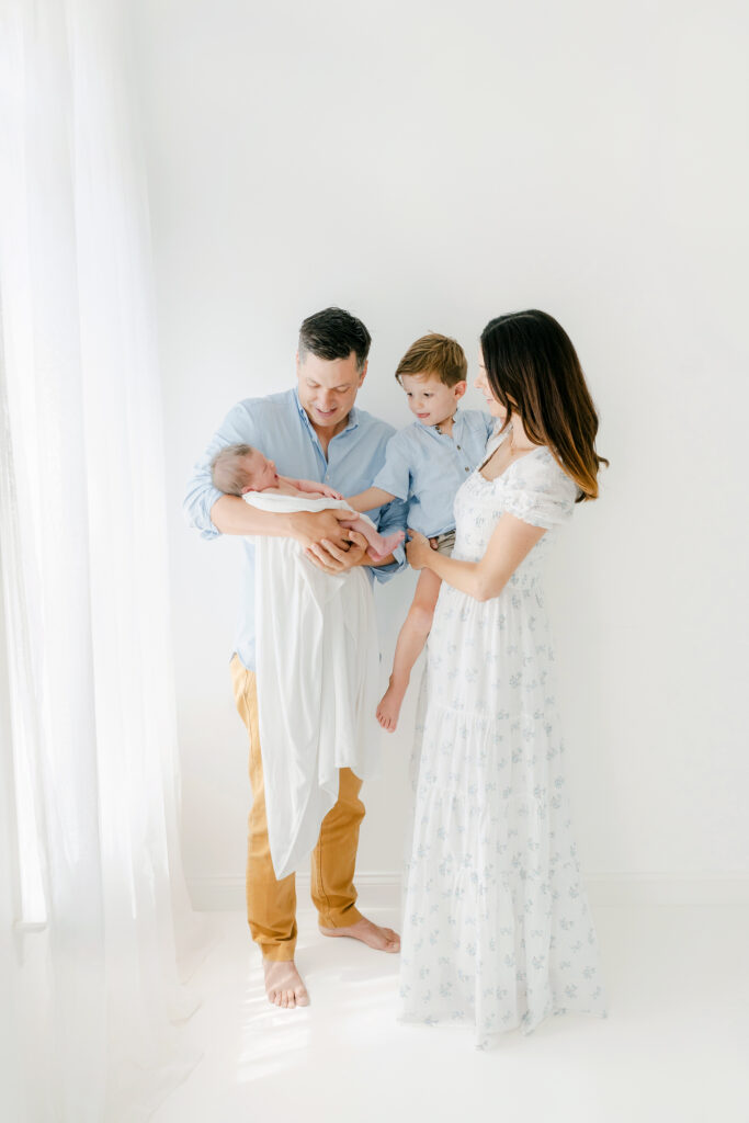 family of 4 pose for a newborn session in a white studio